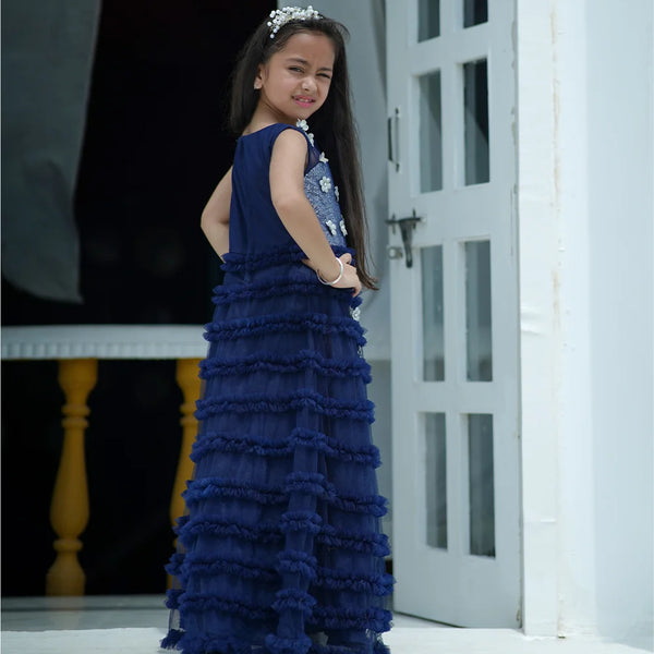 Young girl in a blue ruffled dress standing in a doorway.