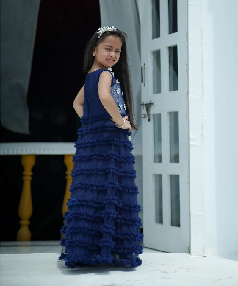Young girl in a blue ruffled dress standing in a doorway.