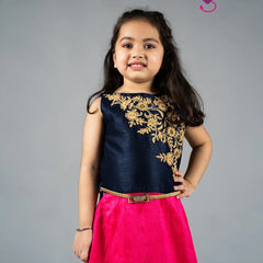 Young girl wearing a navy blue top with gold embroidery and a pink skirt on a gray background
