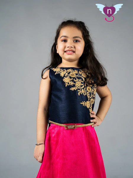 Young girl wearing a navy blue top with gold embroidery and a pink skirt on a gray background