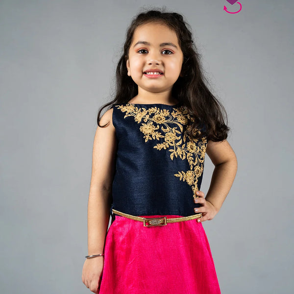 Young girl wearing a navy blue top with gold embroidery and a pink skirt on a gray background