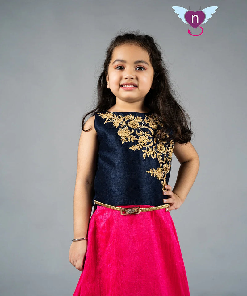 Young girl wearing a navy blue top with gold embroidery and a pink skirt on a gray background