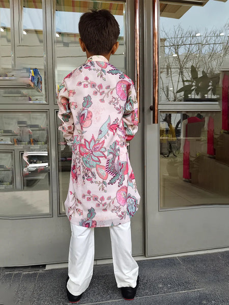 Person wearing a colorful floral kurta with white pants standing in front of a glass door.