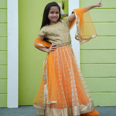 Young girl in an orange and gold traditional outfit standing against a green wall.