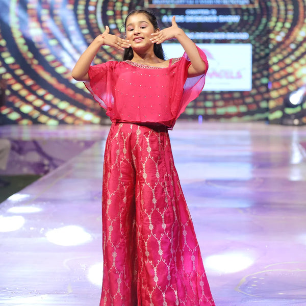 Person in a pink sharara on a stage with a colorful background