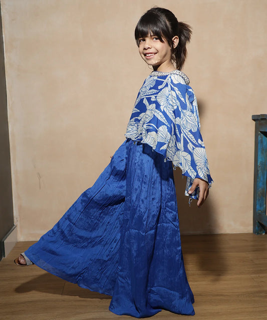 This blue coloured Indian party wear dress for kids consists of a printed cape style top that comes with a back closure and a matching pleated sharara. It features embroidered detailing on the neck and coin detailing at the bottom of the crop top.
