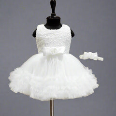 A white sleeveless baby birthday party frock displayed on a mannequin, featuring a bow at the waist and a matching bow for the head.