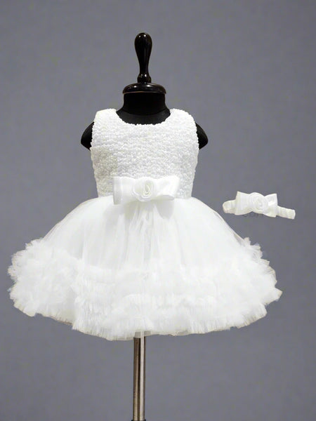 A white sleeveless baby birthday party frock displayed on a mannequin, featuring a bow at the waist and a matching bow for the head.