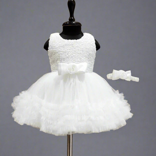 A white sleeveless baby birthday party frock displayed on a mannequin, featuring a bow at the waist and a matching bow for the head.