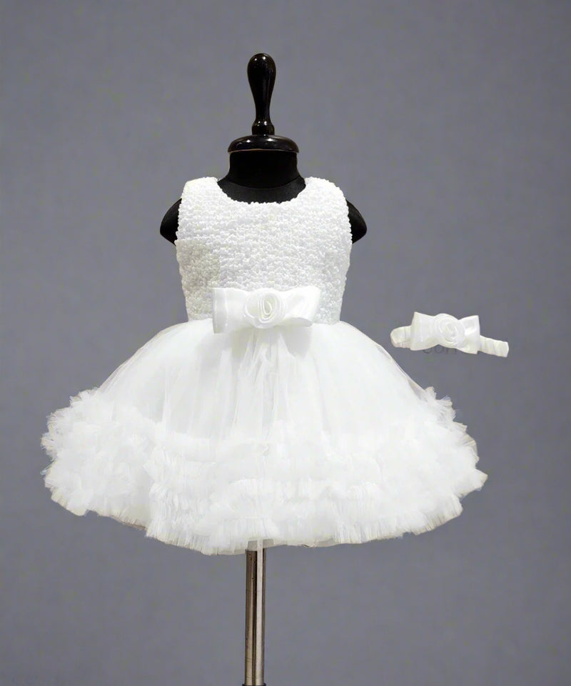 A white sleeveless baby birthday party frock displayed on a mannequin, featuring a bow at the waist and a matching bow for the head.