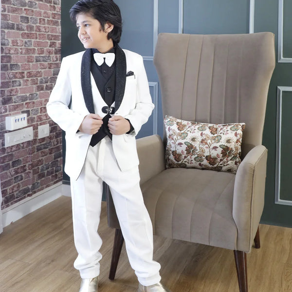 This black and white coloured coat suit for boys consists of a coat, matching pants, a dual-style waistcoat, and a self-textured shirt. It features a matching bow, a cute broach, a pocket square and shimmer detailing on the collar that adds grace to the look.