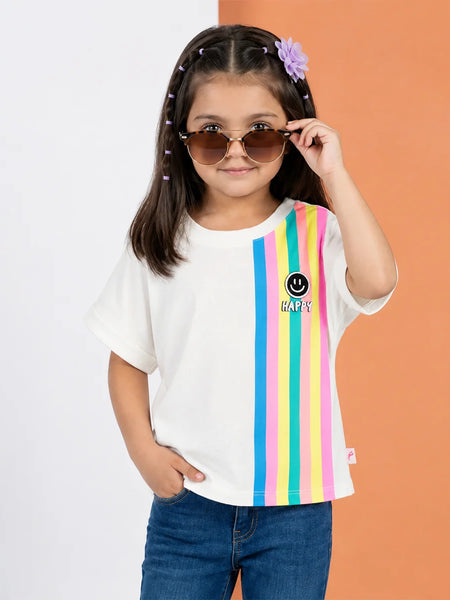 A young girl with sunglasses and a purple flower hair clip wears a white t-shirt with vertical rainbow stripes on the right side and a smiley face logo with 'KAPY' text. She is paired with blue jeans, standing against a split white and orange background.