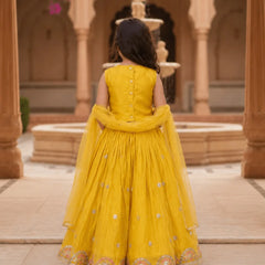 Child in a yellow traditional outfit standing in an architectural setting with columns and a fountain.