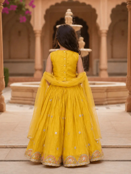 Child in a yellow traditional outfit standing in an architectural setting with columns and a fountain.