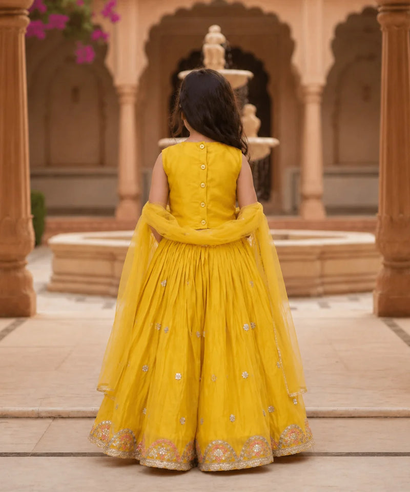 Child in a yellow traditional outfit standing in an architectural setting with columns and a fountain.